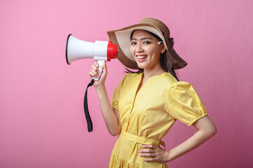 Asian woman smiling brightly while holding a megaphone near her face, wearing a yellow dress and...