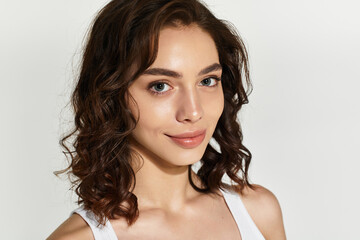 Naklejka premium Young woman with elegant makeup poses gracefully in studio against grey backdrop