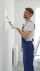 Male professional painter wearing protective white gloves and blue work overalls, applying paint...