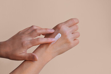 Woman's hand applying hand care cream on soft beige pink background. Female old hands with cosmetic...