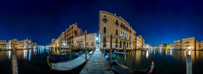 Venice Grand Canal at night with historic buildings, gondolas, and reflections under a starry sky.