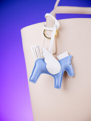 Close-up of a blue leather bag charm in the shape of a cute pegasus with white wings on white bag