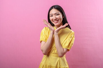 Asian woman wearing a yellow dress smiles warmly while framing her face with both hands under her...