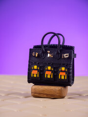 Obraz premium Close-up of a beautiful leather handbag with transparent windows for storing small items and wireless earbuds, set against a purple background