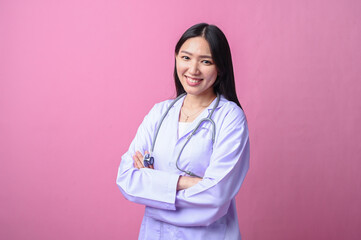 Asian female doctor in white coat and stethoscope smiling confidently with arms crossed, standing...