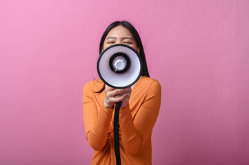 Asian woman with long black hair wearing an orange dress holding a megaphone directly facing the...