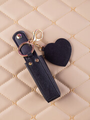 Close-up of a black leather lipstick case with a heart-shaped mirror, elegantly placed on a  beige...
