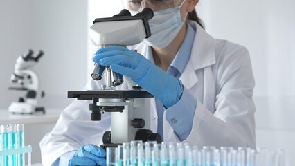 A scientist in protective gear adjusts a microscope lens and accurately analyzes medical research...