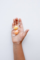 Child hand holding wrapped candy in a caucasian young hand on white background
