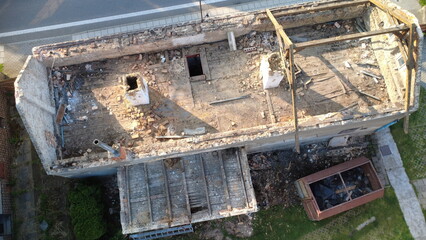 Fototapeta premium Aerial view of the reconstruction and partial demolition of an old brick house. Wooden roof beams are being dismantled, with debris scattered around the site.