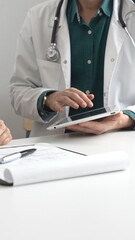 Male doctor in lab coat over a green shirt, and stethoscope gesturing while explaining diagnosis to...