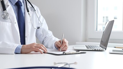 Male doctor writing a prescription and filling out medical records on a clipboard in an office...