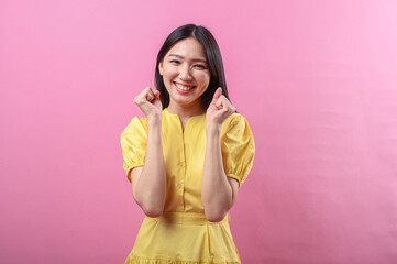 Asian woman in a yellow dress smiling confidently while raising both fists in a celebratory pose....