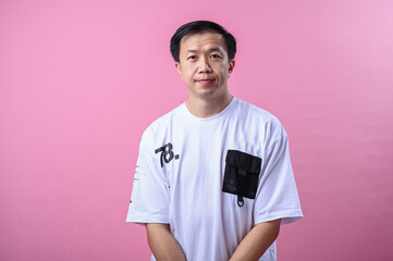 Asian man in white t-shirt standing calmly with a neutral expression in front of a pink background