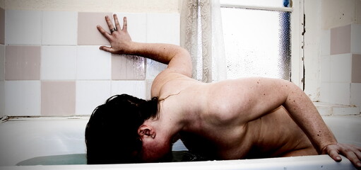 A person submerged in a bathtub, with their head underwater and arm resting on the wall.