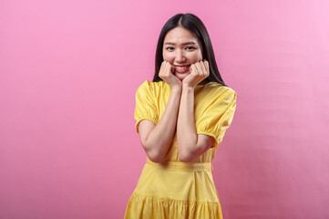 Asian woman wearing a bright yellow dress makes a cute pose with both fists gently resting on her...