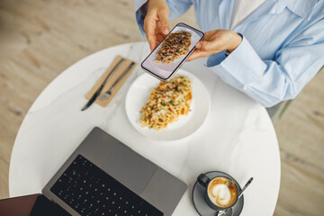 An individual takes a photo of their delicious food while working on a laptop, merging tech with...