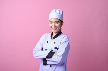Asian female chef in a professional uniform posing confidently with crossed arms, smiling at the...