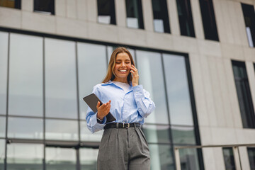 A young woman radiating confidence as she engages with her phone outside a contemporary, modern...