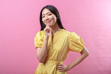 Asian woman in a yellow dress smiling gently with her hand resting under her chin, posing...