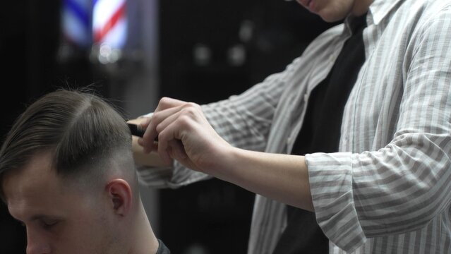 Professional barber carefully combing client's hair, preparing precise hairstyle with expert grooming techniques in modern barbershop setting