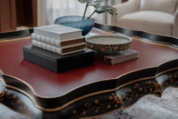Elegant chinoiserie coffee table with red leather top. Stack of books and a porcelain bowl create a classic, luxurious scene.