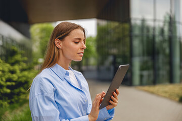 A young woman focuses on a tablet in a stylish outdoor space, blending technology and nature...