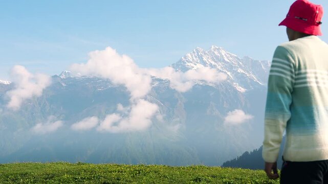 Two male hikers walk through the mountains under drifting clouds. The adventurous travelers reach the top of the mountain and wait for the sunset at Buda Madmaheshwar, Uttarakhand, India.	