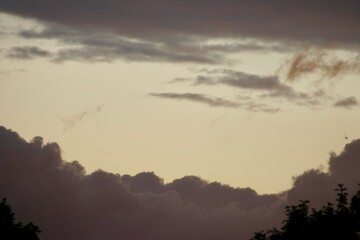 Dramatic evening sky with dense clouds and a soft dark glow from the setting sun, above dark...