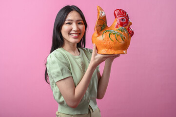 Asian woman smiling while lifting a large orange ceramic rooster to shoulder level with both hands...