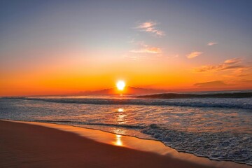 A sunset on the beach with waves and sand