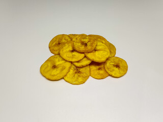 A pile of golden, crispy plantain chips arranged on a plain white surface, showcasing their texture...