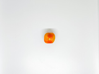 A single, small, square-shaped tomato sits centered on a plain white surface, casting a soft shadow...