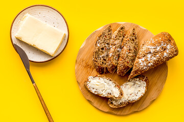 Traditional breakfast. Wholegrain bread on cutting board with butter on plate on yellow background...