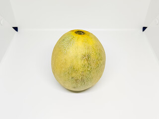 A single, whole cantaloupe melon with a textured rind, centered on a white surface, under bright...