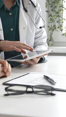 Doctor man in lab coat over a green shirt, and stethoscope is using tablet while consulting patient...