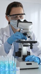 Female scientist examining microscope slide, wearing protective gear in laboratory, researching...