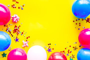 Party concept. Colorful balloons and confetti on yellow background top-down frame copy space