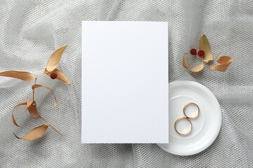 Wedding invitation card, golden rings and dry leaves on grey tulle cloth, top view
