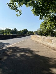 View looking across an old Roman single lane road bridge in bright sunlight with shadows being formed.