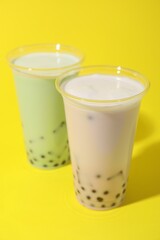Tasty milk bubble tea in plastic cups on yellow background