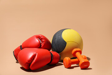 Medicine ball, dumbbells and boxing gloves on beige background