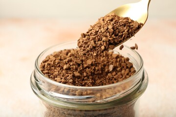 Taking granulated instant coffee from jar with spoon on blurred light background, closeup