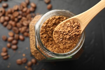 Spoon with granulated instant coffee, jar and beans on dark table, top view