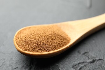 Spoon with instant coffee powder on dark textured table, closeup