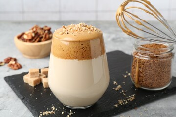 Delicious dalgona coffee in glass, brown sugar, walnuts, whisk and granules on grey table, closeup