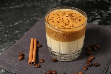 Delicious dalgona coffee in glass, beans and cinnamon on dark marble table, closeup