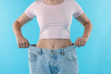 Woman wearing old jeans after weight loss on light blue background, closeup