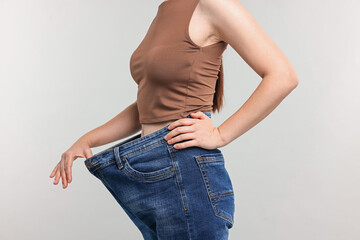 Woman wearing old jeans after weight loss on light grey background, closeup
