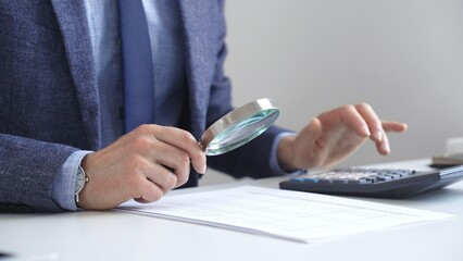 Businessman financial analyst is analyzing financial documents with a calculator and magnifying...